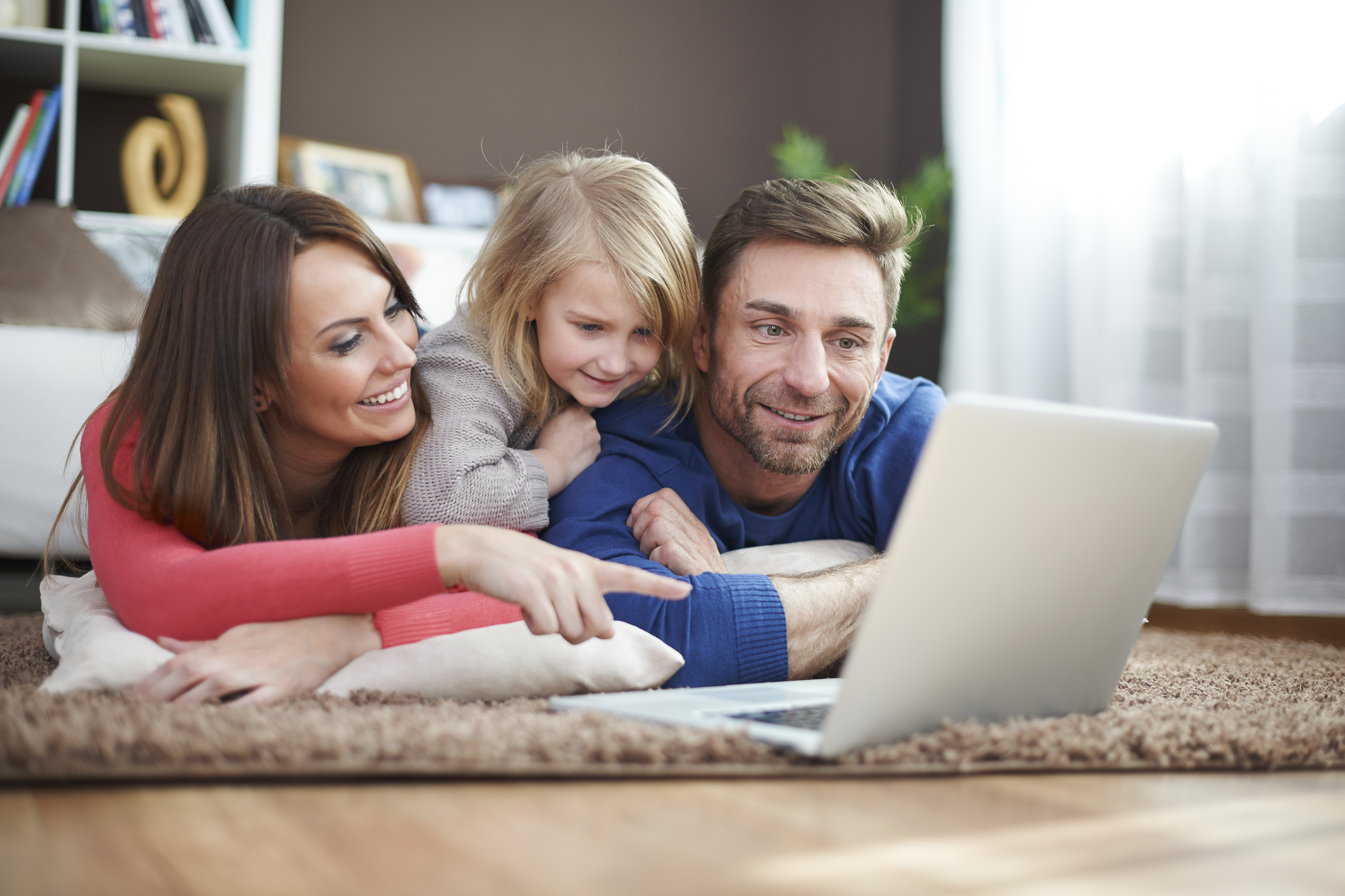 A mother daughter and dad laying happily viewing a computer screen.