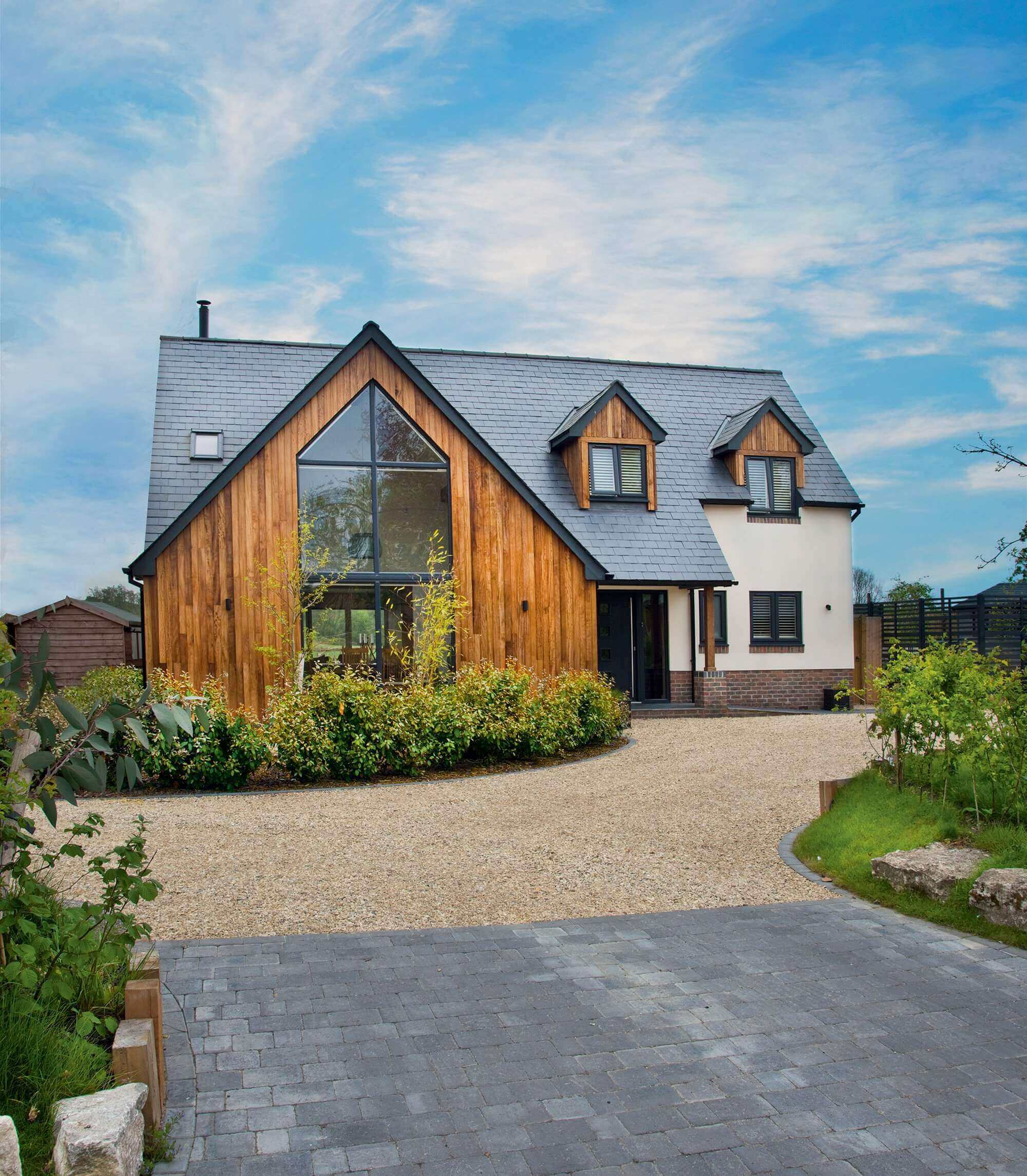 A fully finished timber frame house with a long drive away towards the house.